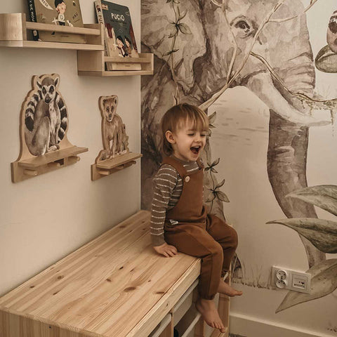 1. Child sitting on a wooden bench next to Dekornik mini wall shelf with lemur design in a decorated room