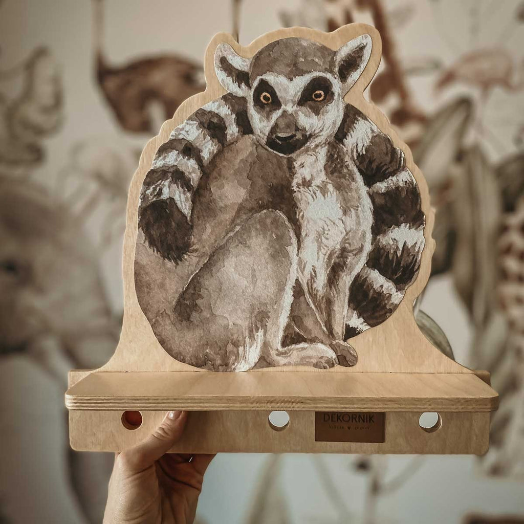 2. Hand holding Dekornik mini wall shelf with lemur design, showing plywood material and brand logo