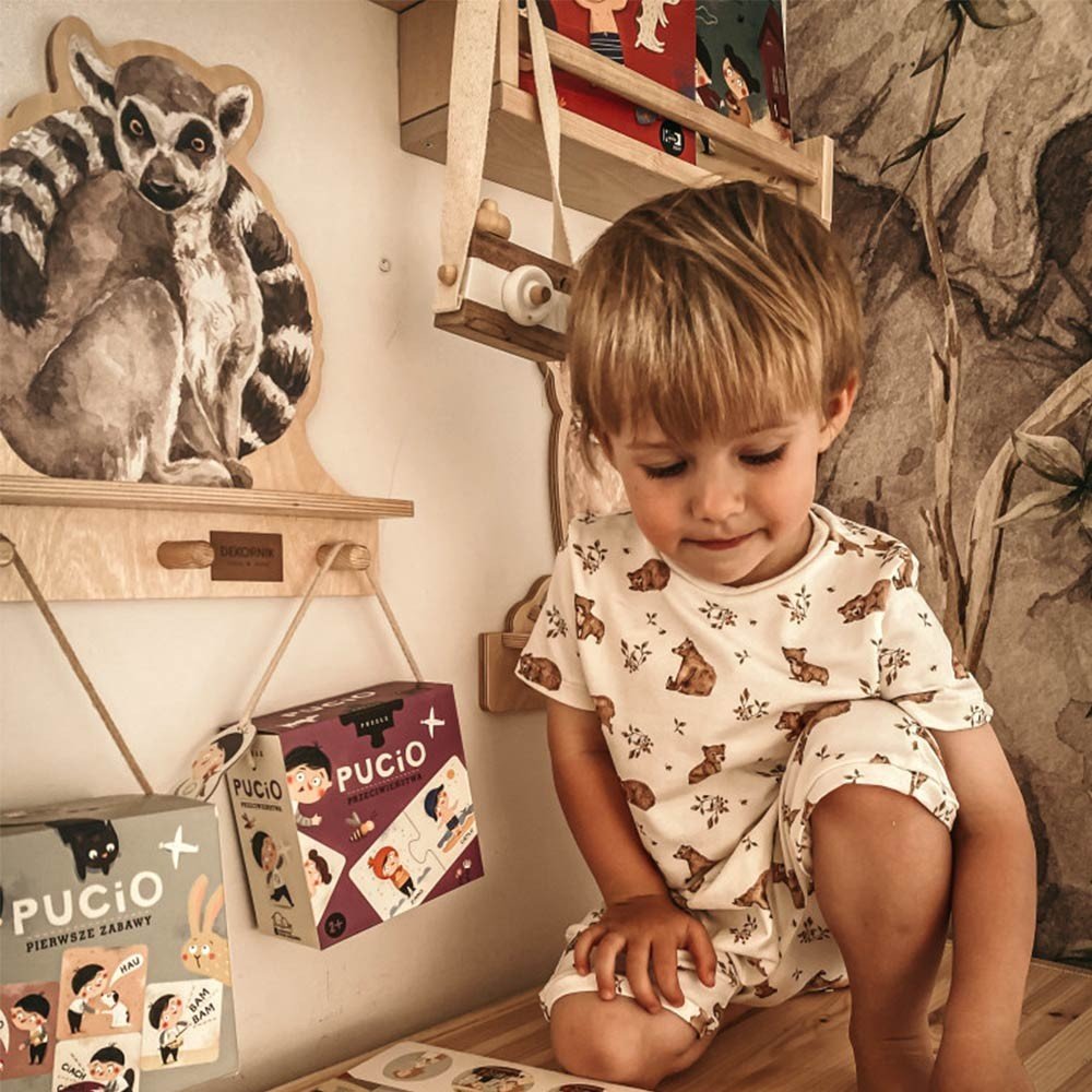 1. Child sitting near Dekornik mini wall shelf with lemur design, surrounded by books and toys