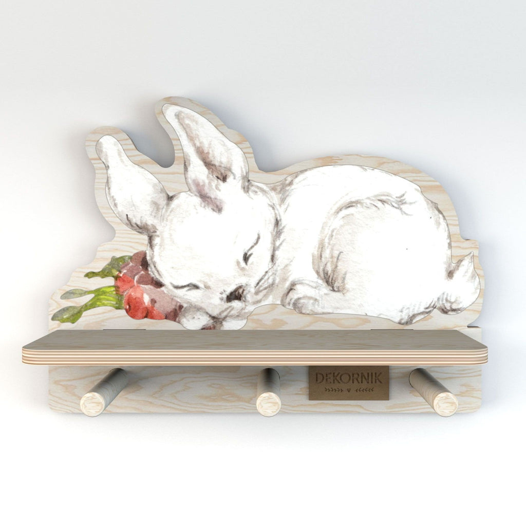 1. Dekornik mini wall shelf with sleeping rabbit design, featuring three wooden pegs and a horizontal shelf, made of bright plywood with a printed sticker, shown in a studio setting
