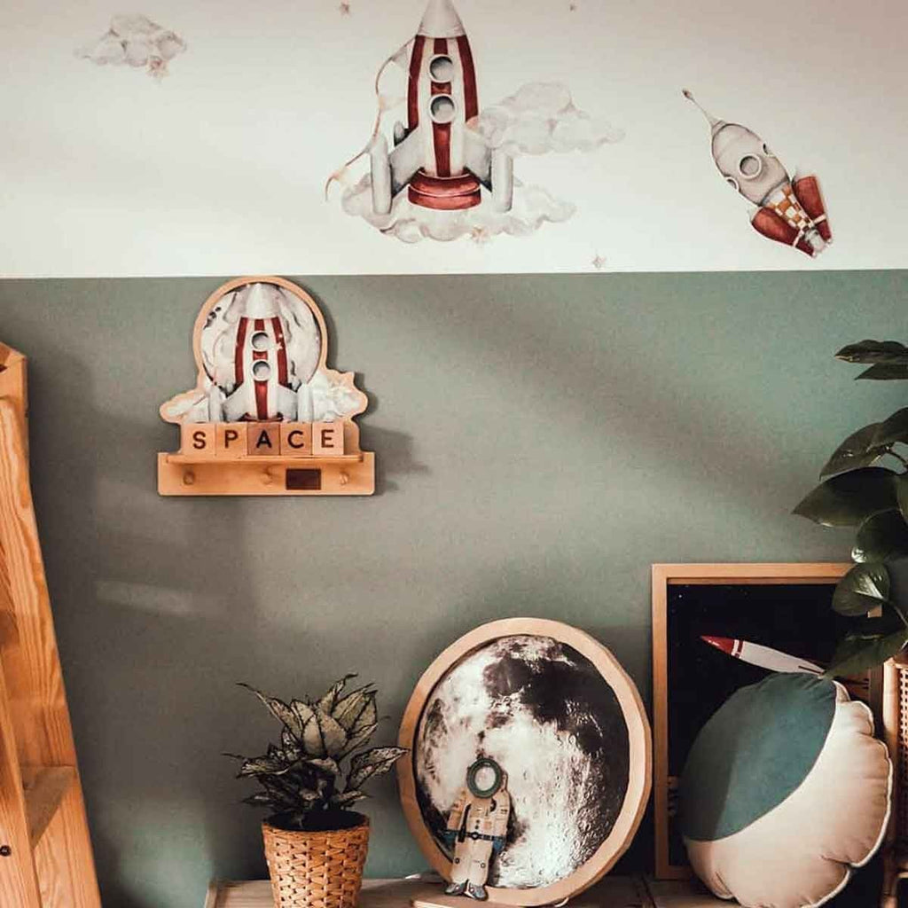 4. Rocketship mini wall shelf with pegs, mounted on a green wall with space-themed decor, including a globe and astronaut figure.