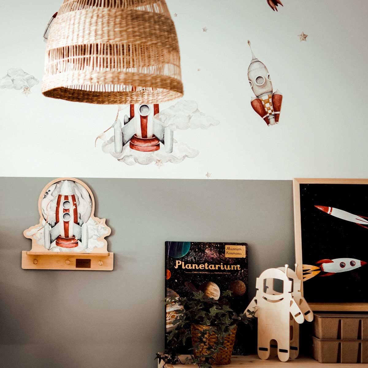 7. Rocketship mini wall shelf with pegs, part of a space-themed room decor with books and astronaut figure, under a wicker lamp.