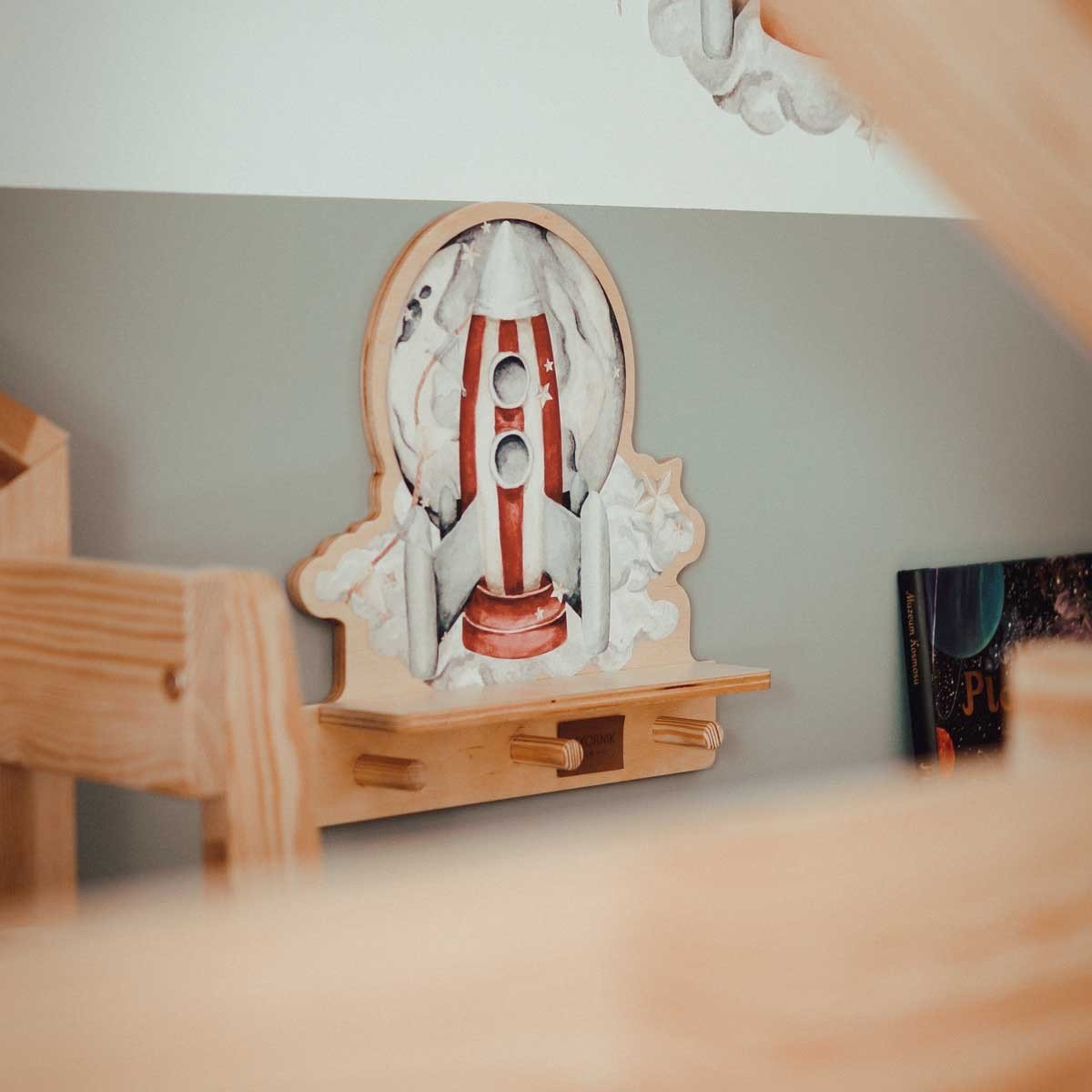 6. Rocketship mini wall shelf with pegs, mounted on a wall in a child's room, partially obscured by wooden furniture.