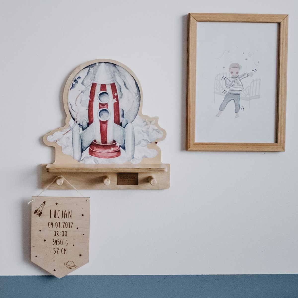 1. Rocketship-themed mini wall shelf with pegs, mounted on a wall next to framed art and a personalized banner, in a child's room setting.
