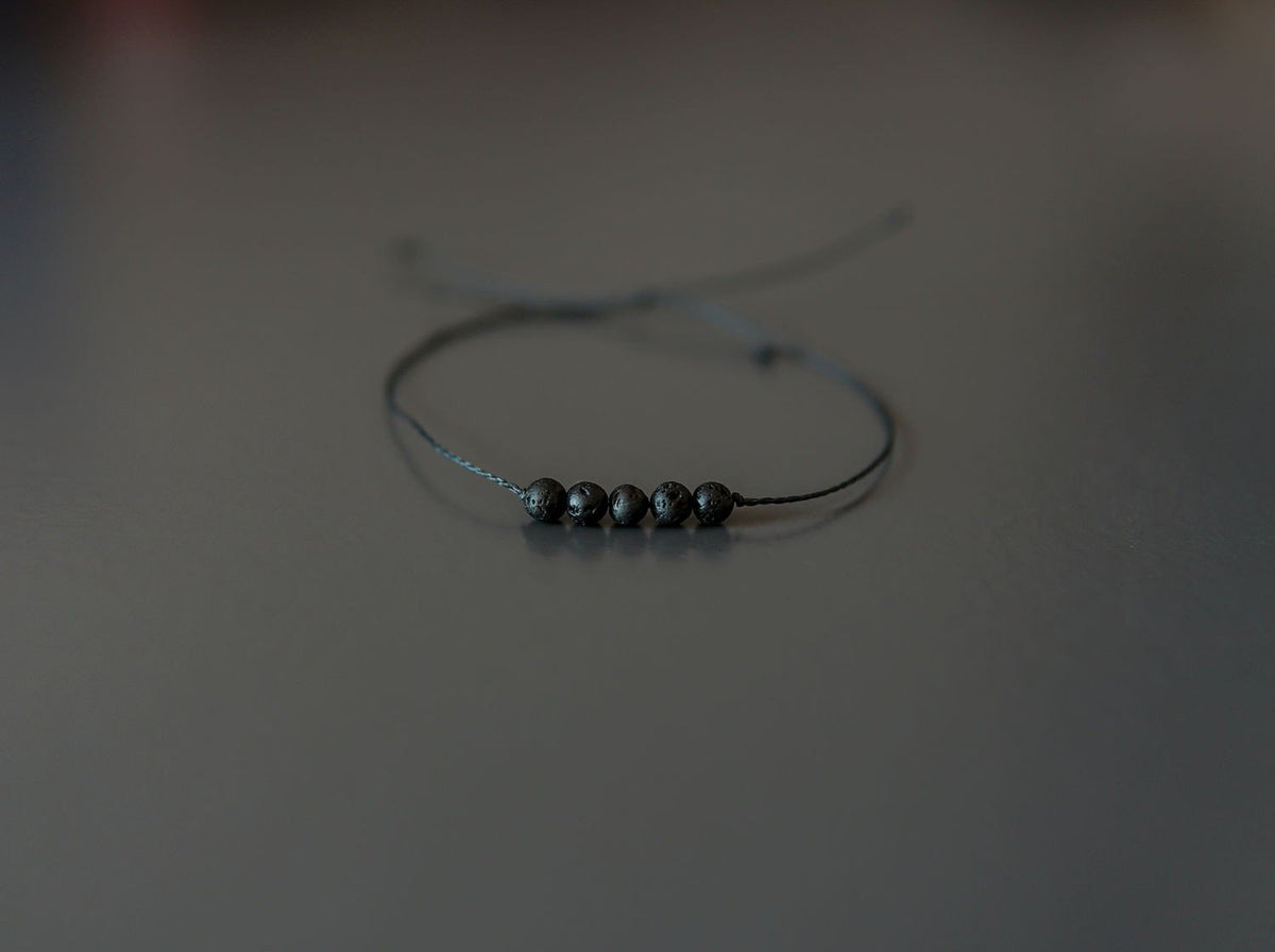 2. Studio shot of Canary Lava minimalist lava stone bracelet with adjustable kevlar string and polished volcanic beads