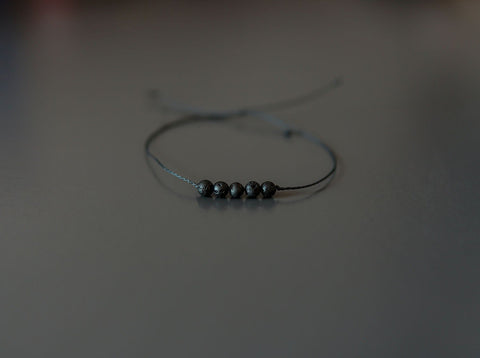 2. Studio shot of Canary Lava minimalist lava stone bracelet with adjustable kevlar string and polished volcanic beads