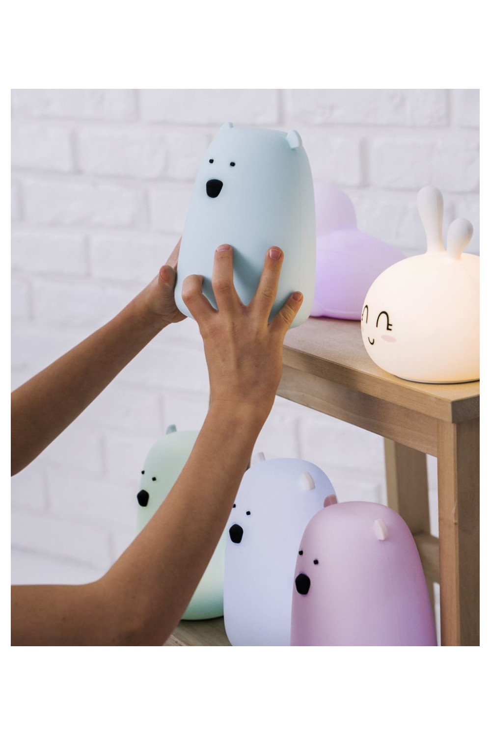 5. Person placing blue Big Bear silicone lamp by Rabbit & Friends on wooden shelf with other lamps