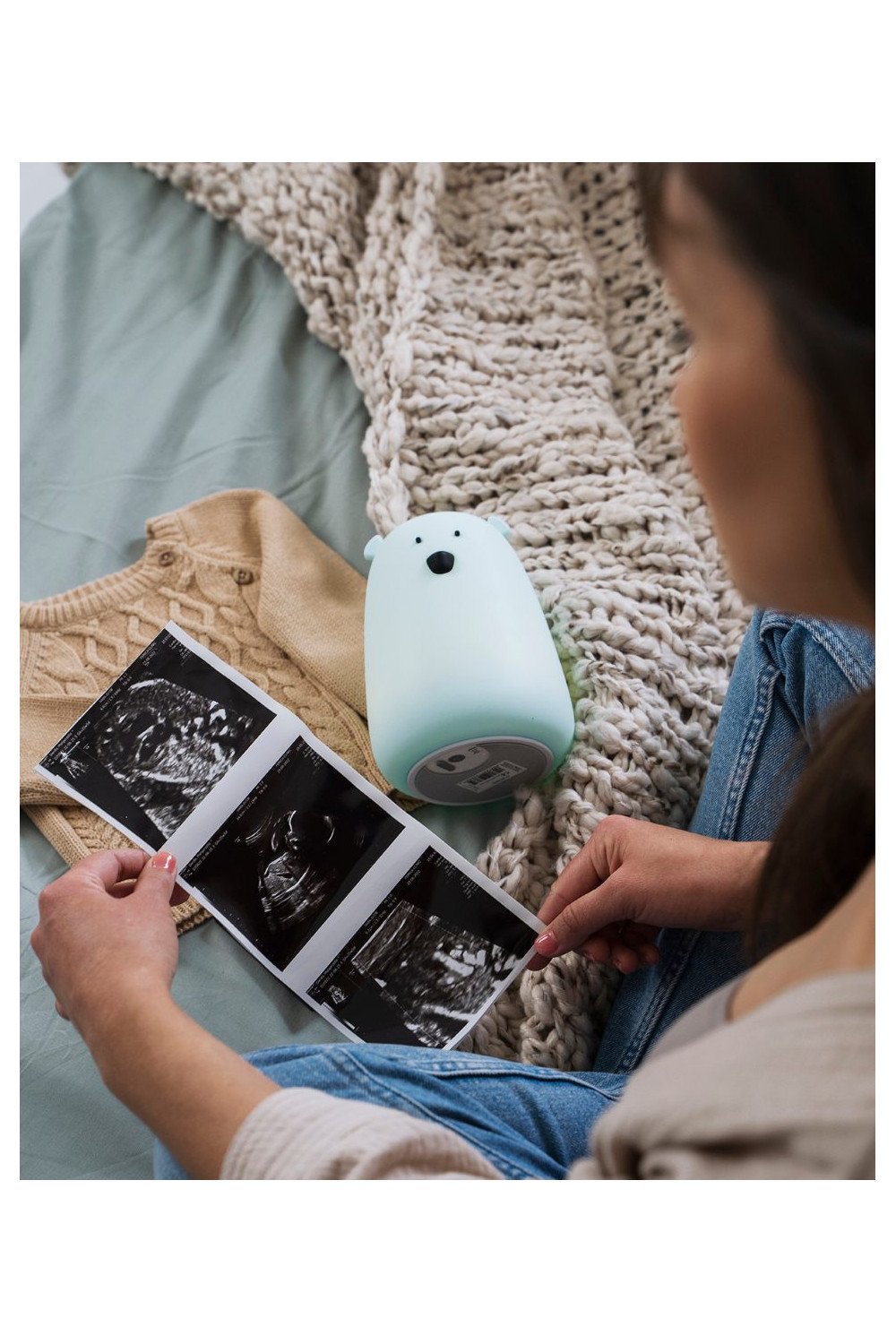 4. Woman looking at ultrasound images with blue Big Bear silicone lamp by Rabbit & Friends on bed