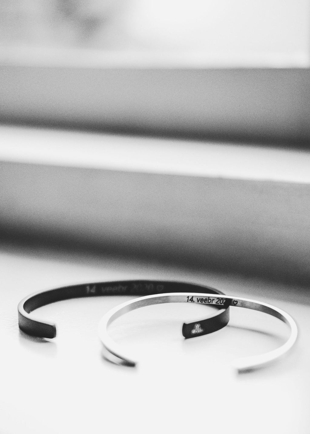 1. Two men's bracelets, one black and one silver, with engraved dates, placed on a windowsill