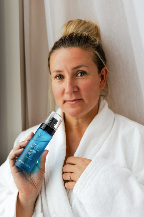 1. Woman in white robe holding Berrichi MIST Face Spray, showcasing product use