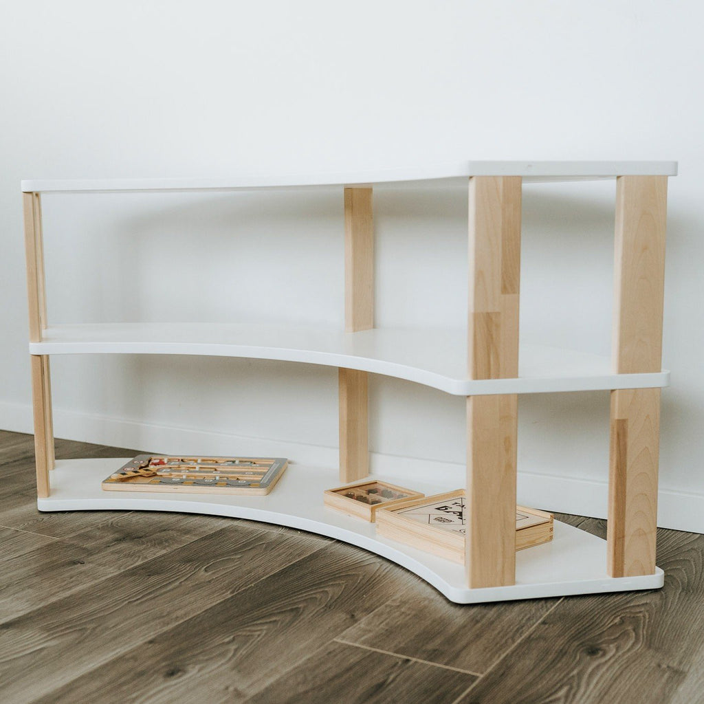4. Modular Montessori shelf with three white shelves and natural wood supports, displaying children's books, on wooden flooring.