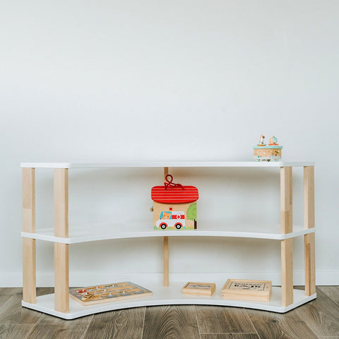 1. Modular Montessori shelf with three white shelves and natural wood supports, featuring children's toys, set against a white wall on wooden flooring.