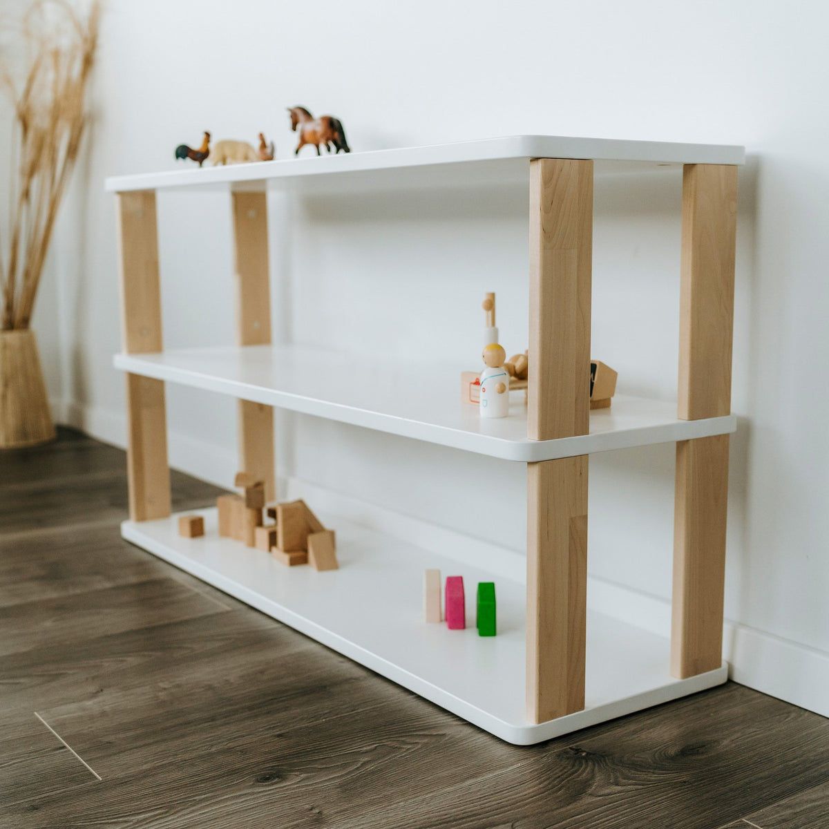 6. White and natural wood Montessori shelf with toys, placed on dark wood flooring near a wall
