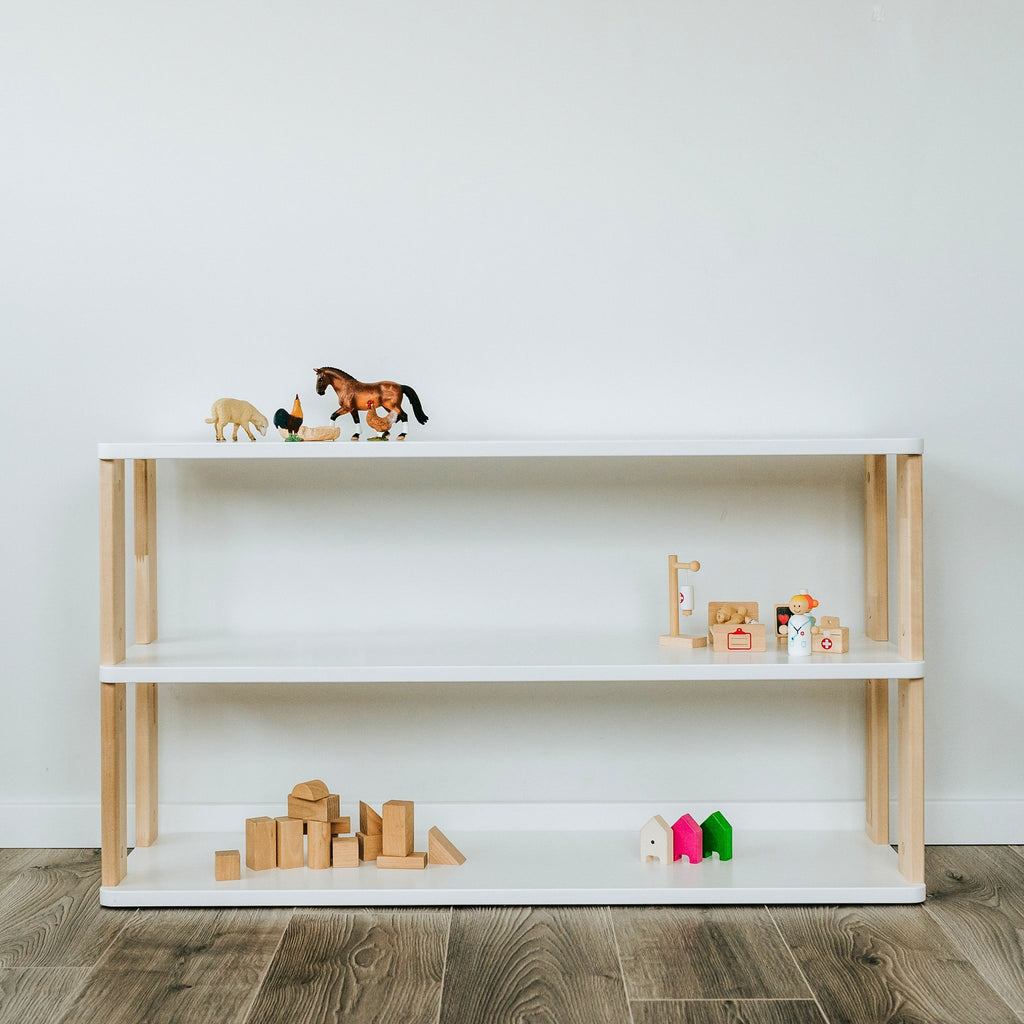 7. White Montessori shelf with natural wood accents, displaying toys, against a white wall on dark wood flooring