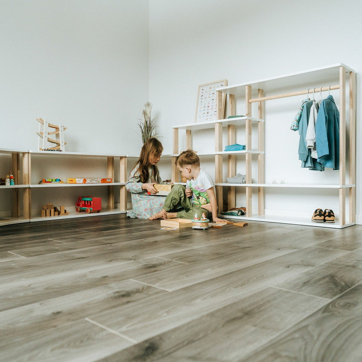2. Two children playing near modular Montessori shelves with toys and clothes in a bright room