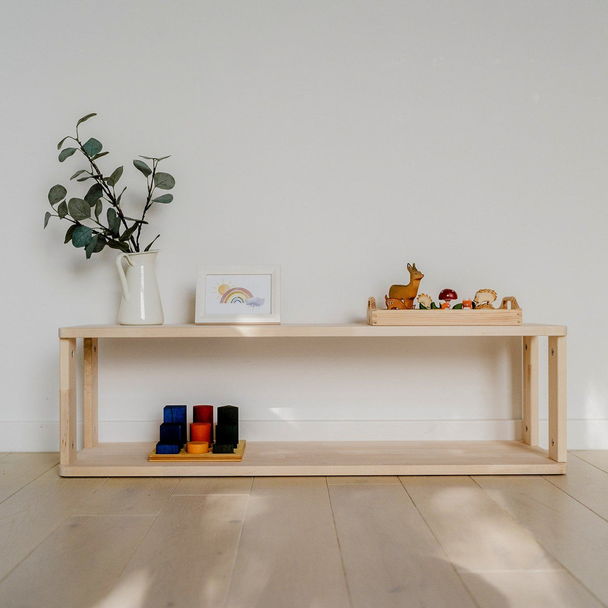 1. Natural wood Montessori shelf with toys and decor on light wood floor against white wall