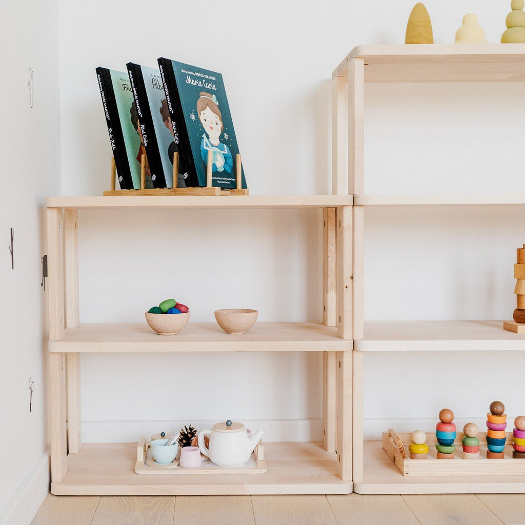 2. Two modular Montessori shelves with books, toys, and bowls, set against a white wall