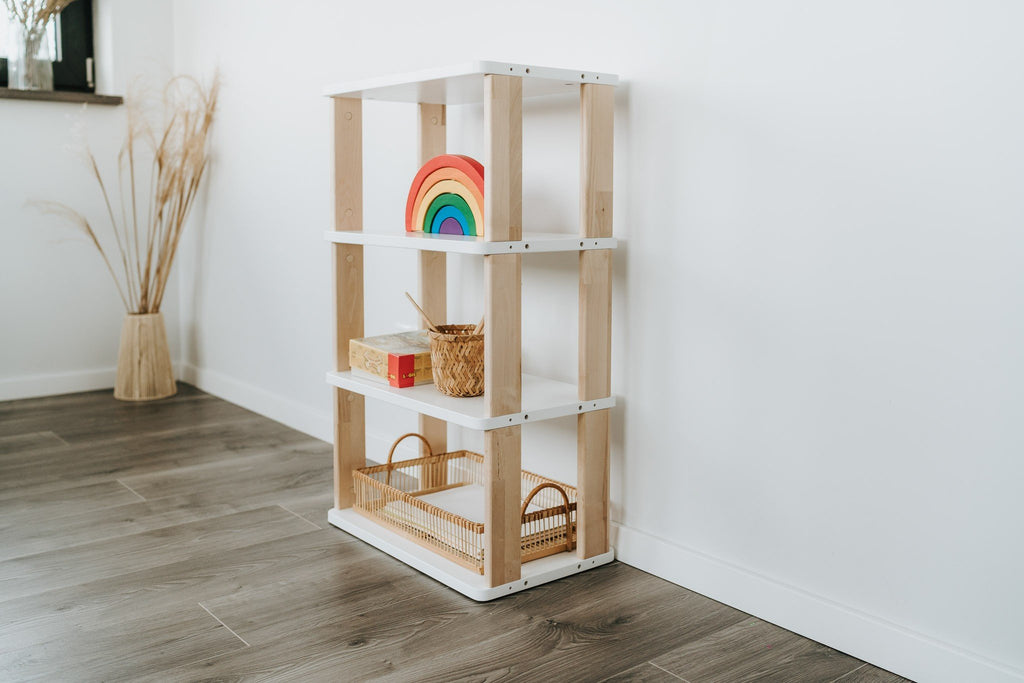 1. Modular Montessori Shelf Straight Mini with four shelves in a children's room, featuring natural wood and white painted finish, holding toys and baskets, against a white wall and wooden floor.
