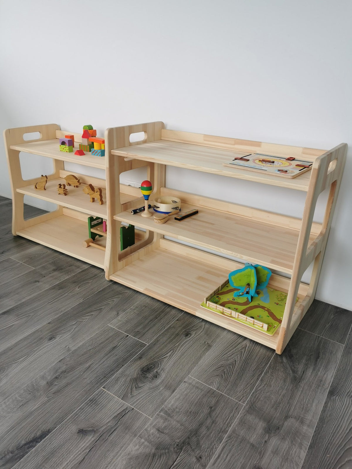 2. Two modular Montessori toy shelves in natural wood on a wooden floor, displaying toys and books