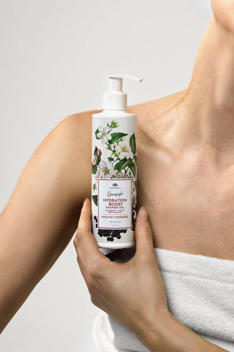 1. Woman holding Magrada Organic Cosmetics moisturizing shower gel with elderberry and jasmine, featuring floral design on bottle, against bare shoulder in minimal setting
