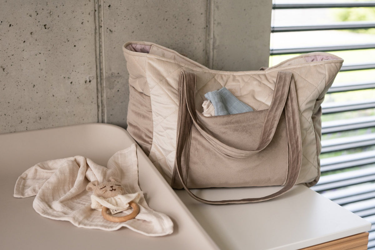 1. Beige mom weekender bag with long straps on a changing table next to baby items
