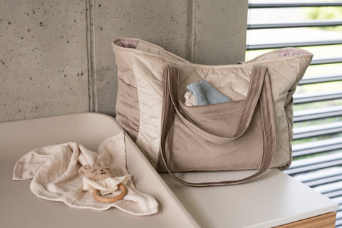 1. Beige mom weekender bag with long straps on a changing table next to baby items