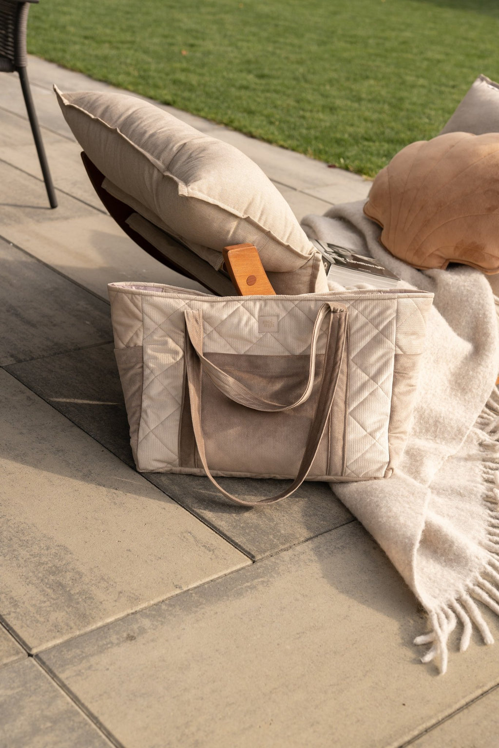 1. Beige mom weekender bag with quilted design and long straps on patio with cushions and blanket