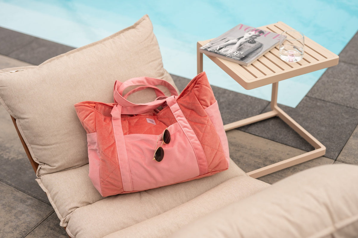 1. Pink quilted weekender bag on a poolside lounge chair with sunglasses and a magazine nearby
