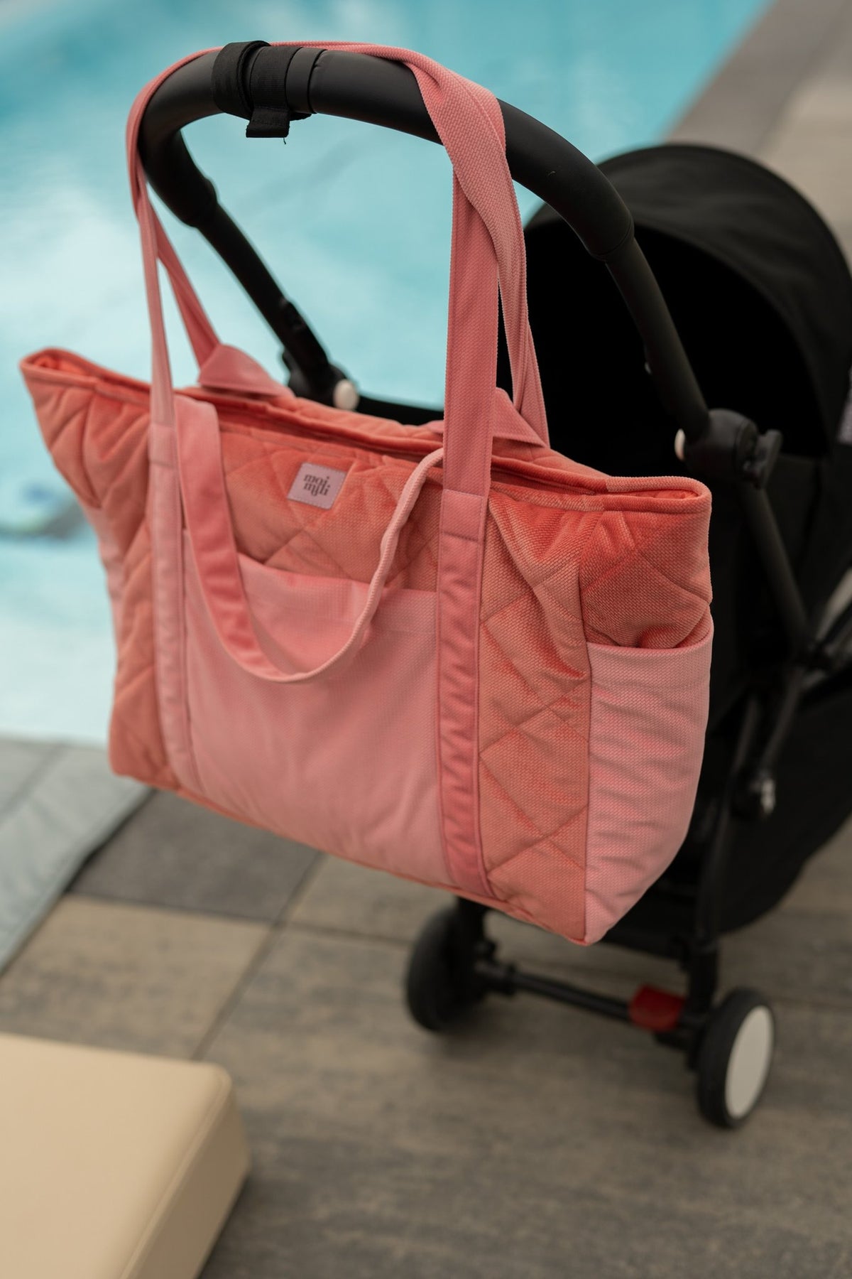 6. Pink quilted weekender bag hanging on a stroller by the pool