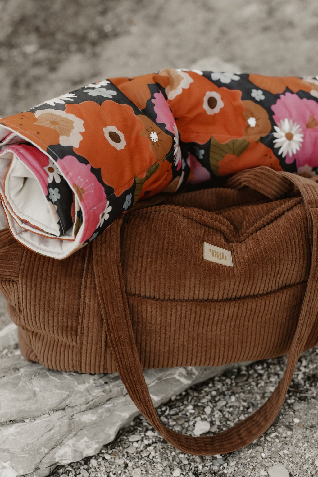 2. Caramel velvet weekender bag with floral blanket on rocky surface