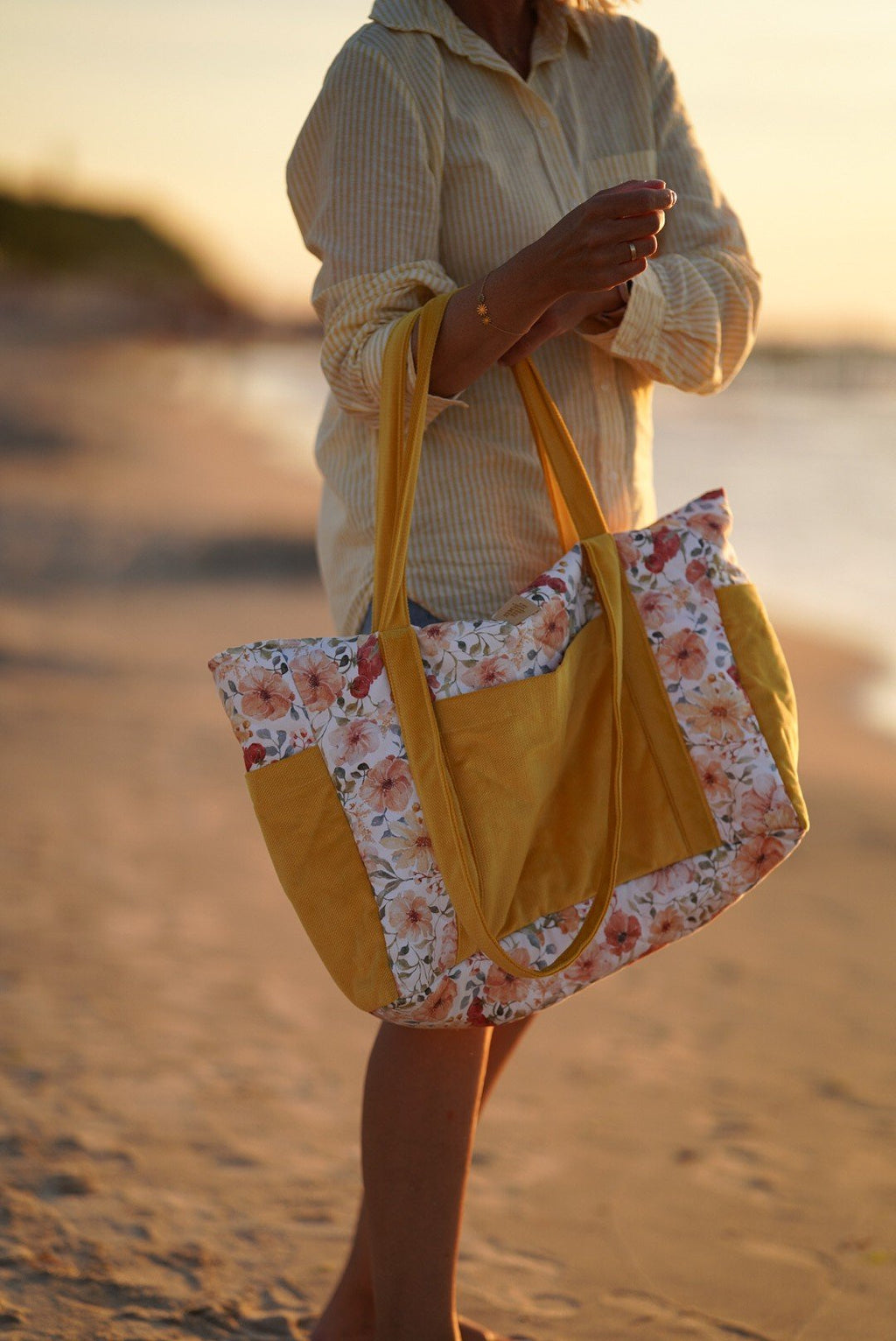 3. Woman carrying yellow and floral weekender bag on beach during sunset
