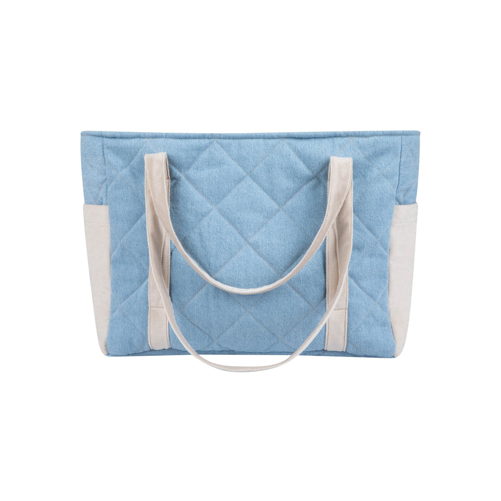 7. Back view of blue quilted weekender bag with beige handles and outer pockets in a studio setting