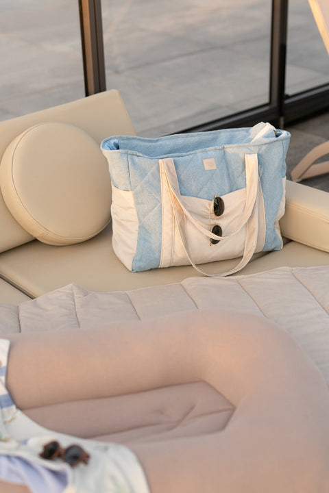 3. Blue and beige weekender bag with buttons on a beige lounge chair in a sunlit outdoor setting