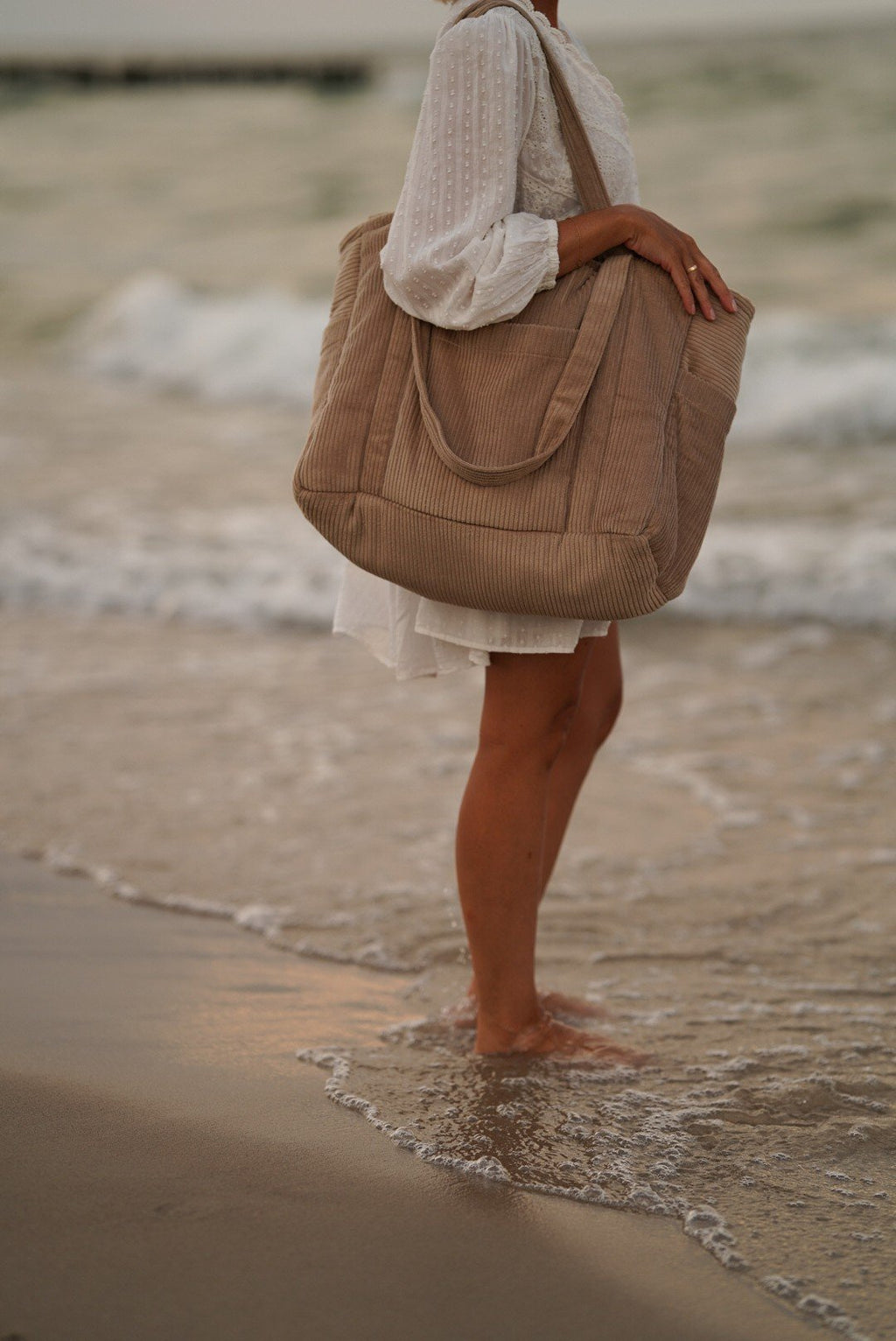 1. Close-up of woman standing in ocean waves holding latte-colored weekender bag