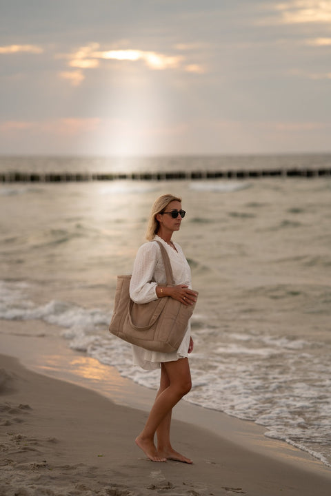 1. Woman walking on beach carrying latte-colored weekender bag, wearing white dress