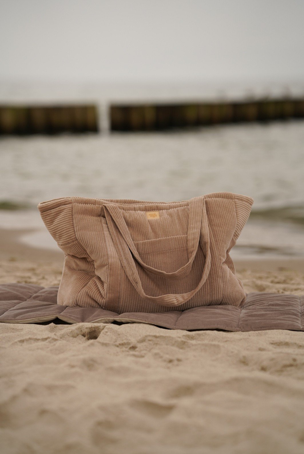 1. Latte-colored weekender bag on beach sand with ocean in background