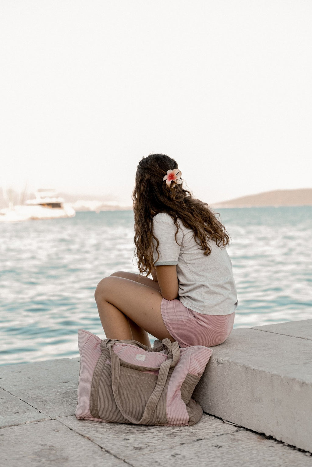 7. Woman sitting on a dock with pink and coffee-colored weekender bag, looking out at the water