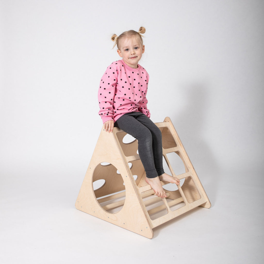 1. Young girl in pink polka dot sweater sitting on top of Montessori 3-angle climber in studio setting