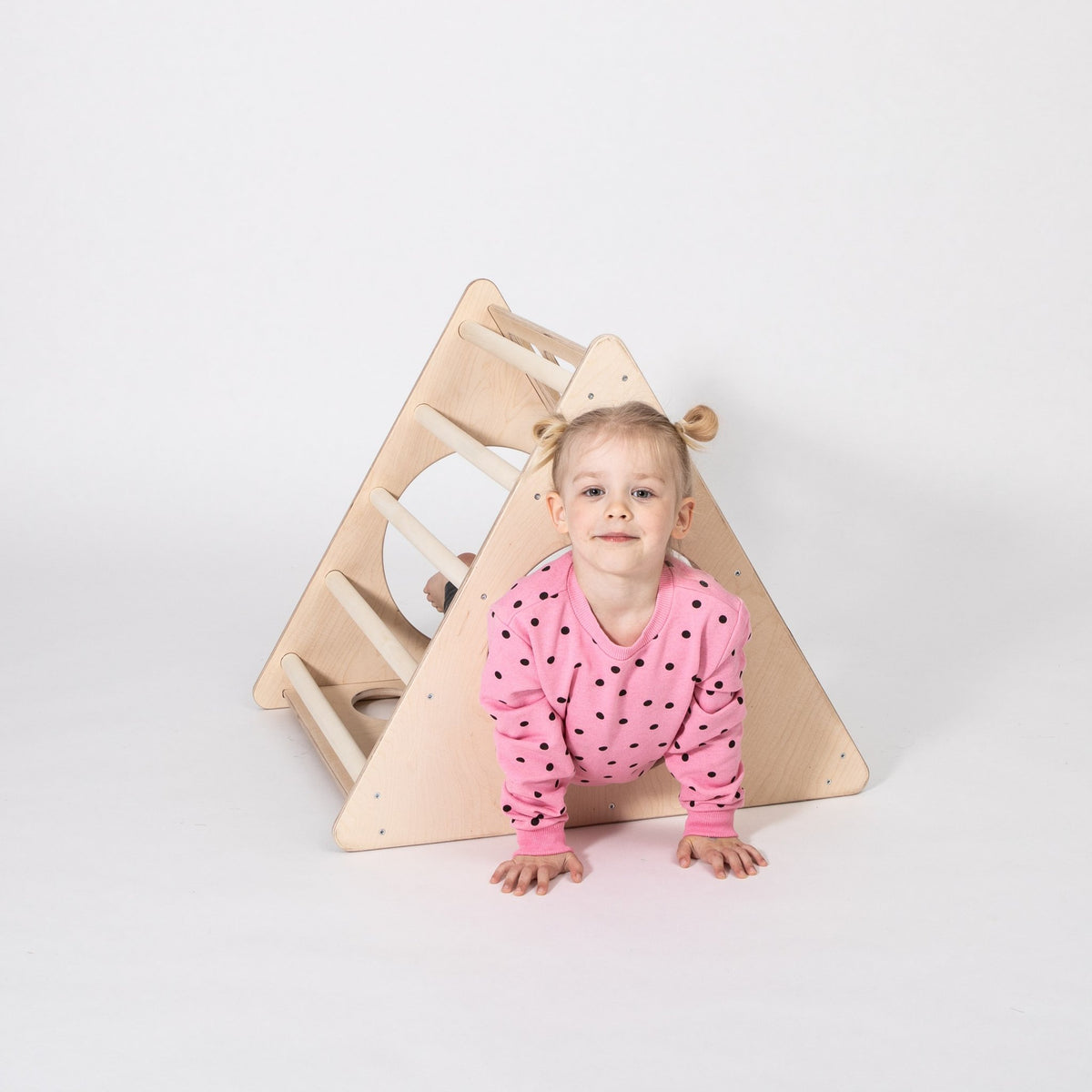 1. Young girl in pink polka dot sweater crawling through Montessori 3-angle climber in studio setting
