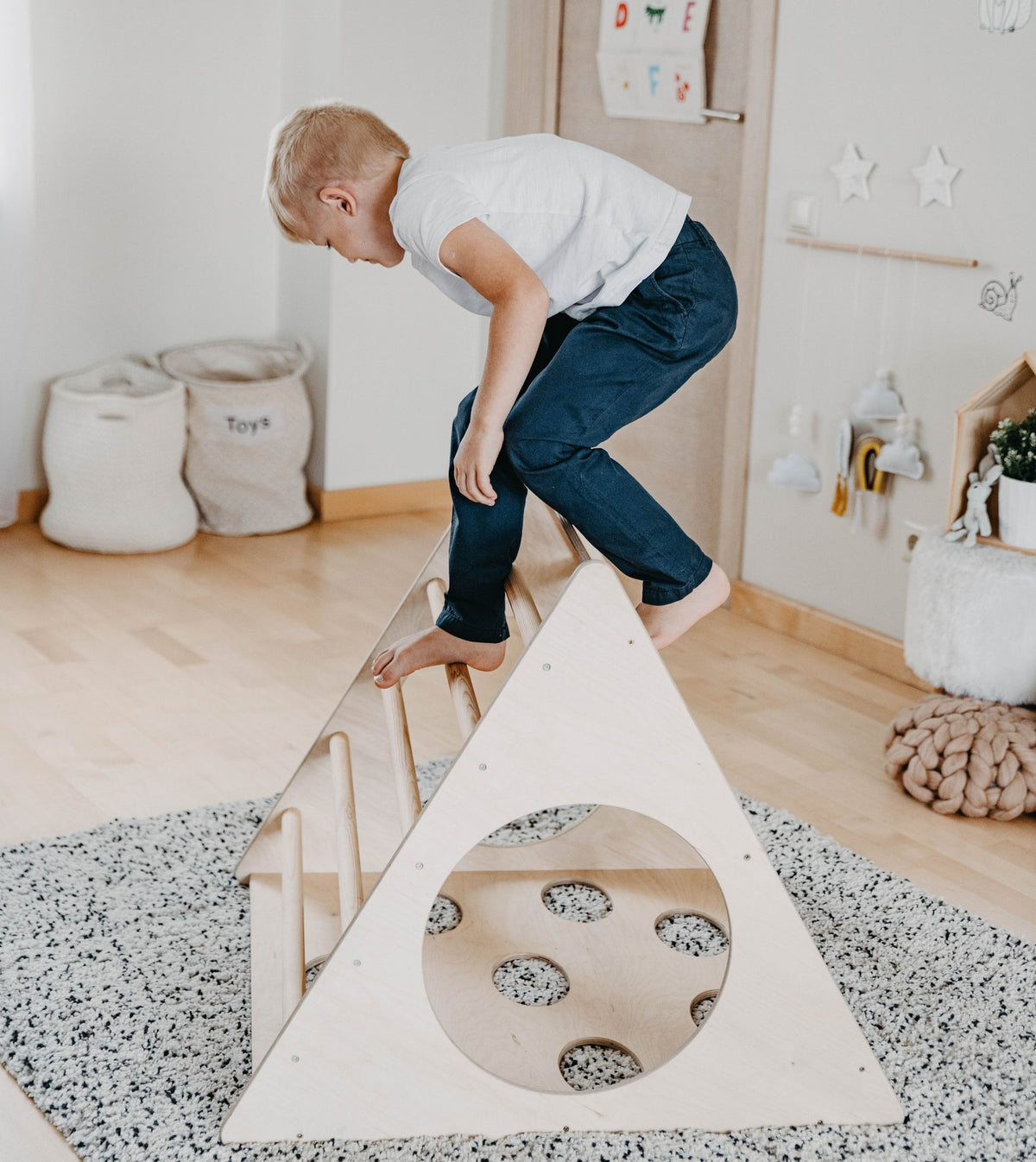 1. Young boy in white shirt climbing Montessori 3-angle climber in a playroom setting