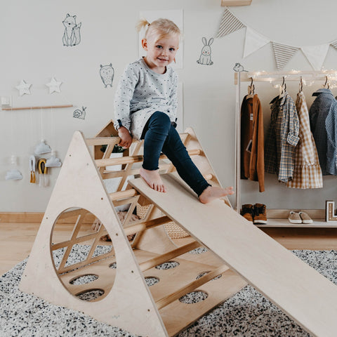 1. Toddler girl in polka dot dress climbing Montessori wooden triangle with ramp in playroom