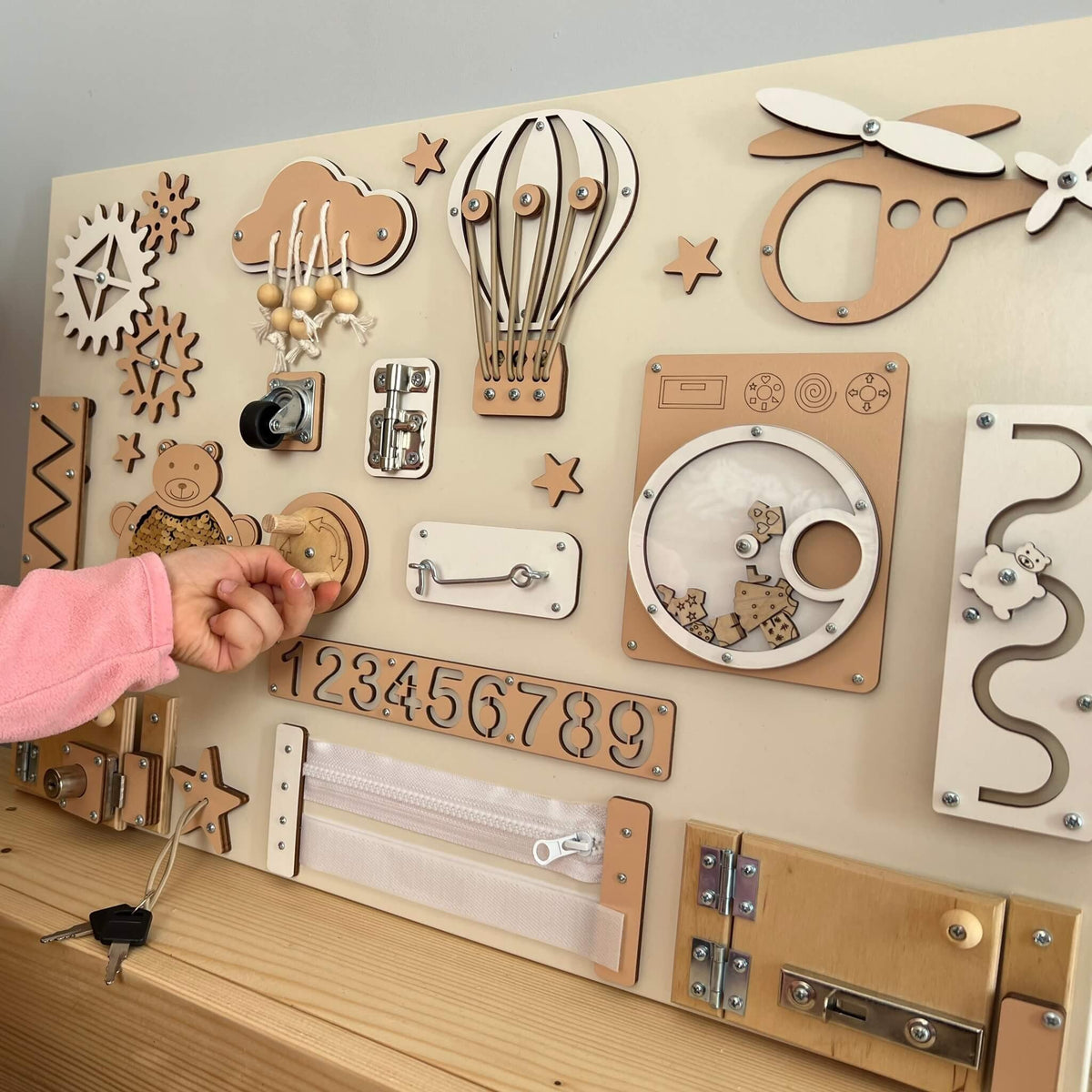 3. Close-up of hand interacting with beige Montessori busy board featuring locks and gears