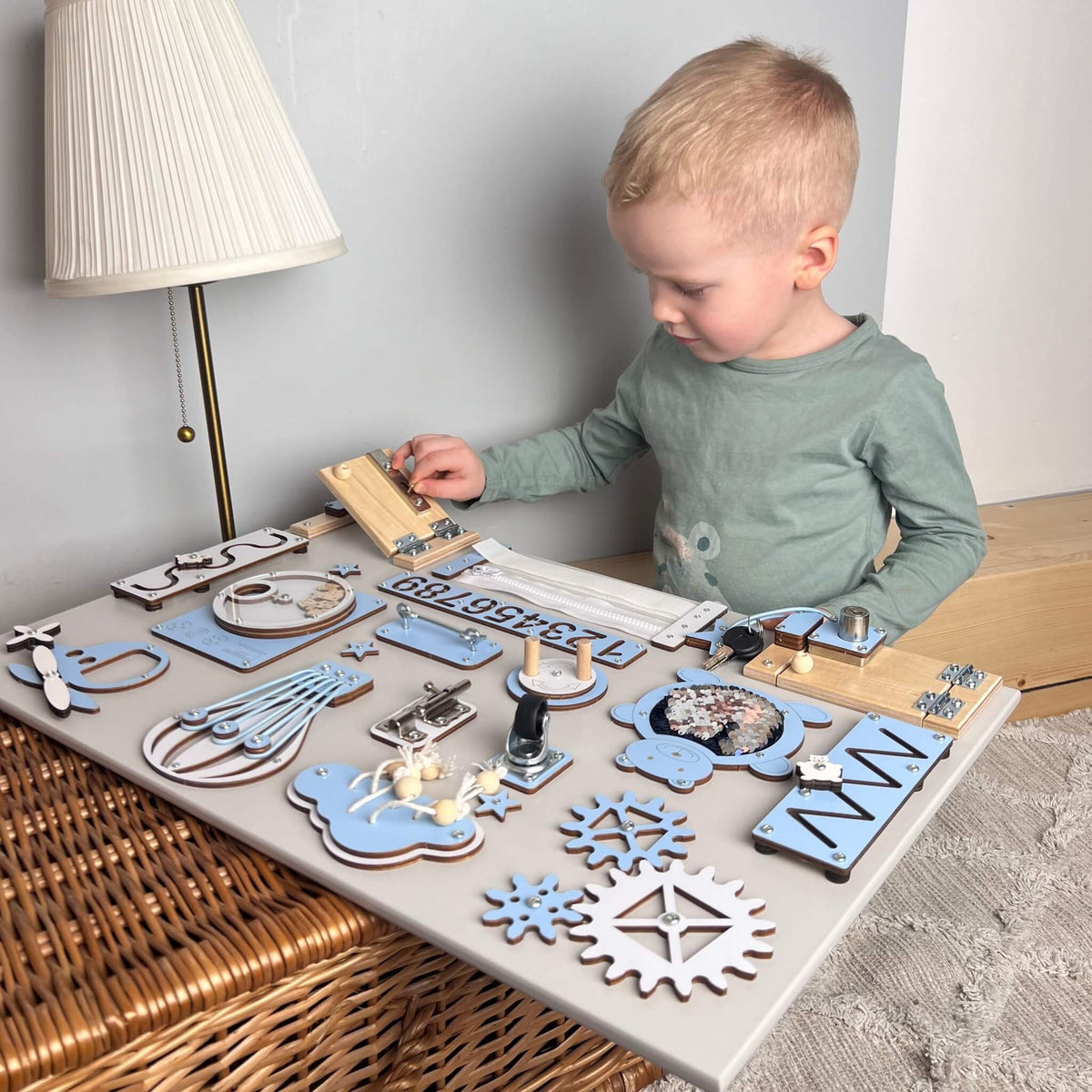 1. Child playing with a blue Montessori busy board featuring locks, gears, and numbers on a wicker table