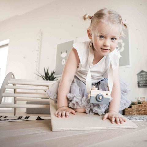4. Young girl climbing a wooden ramp attached to a Montessori climbing arch, wearing a tutu and toy camera in a playful room