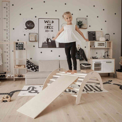 1. Girl in white top and black pants balancing on wooden Montessori climbing arch with ramp in playroom