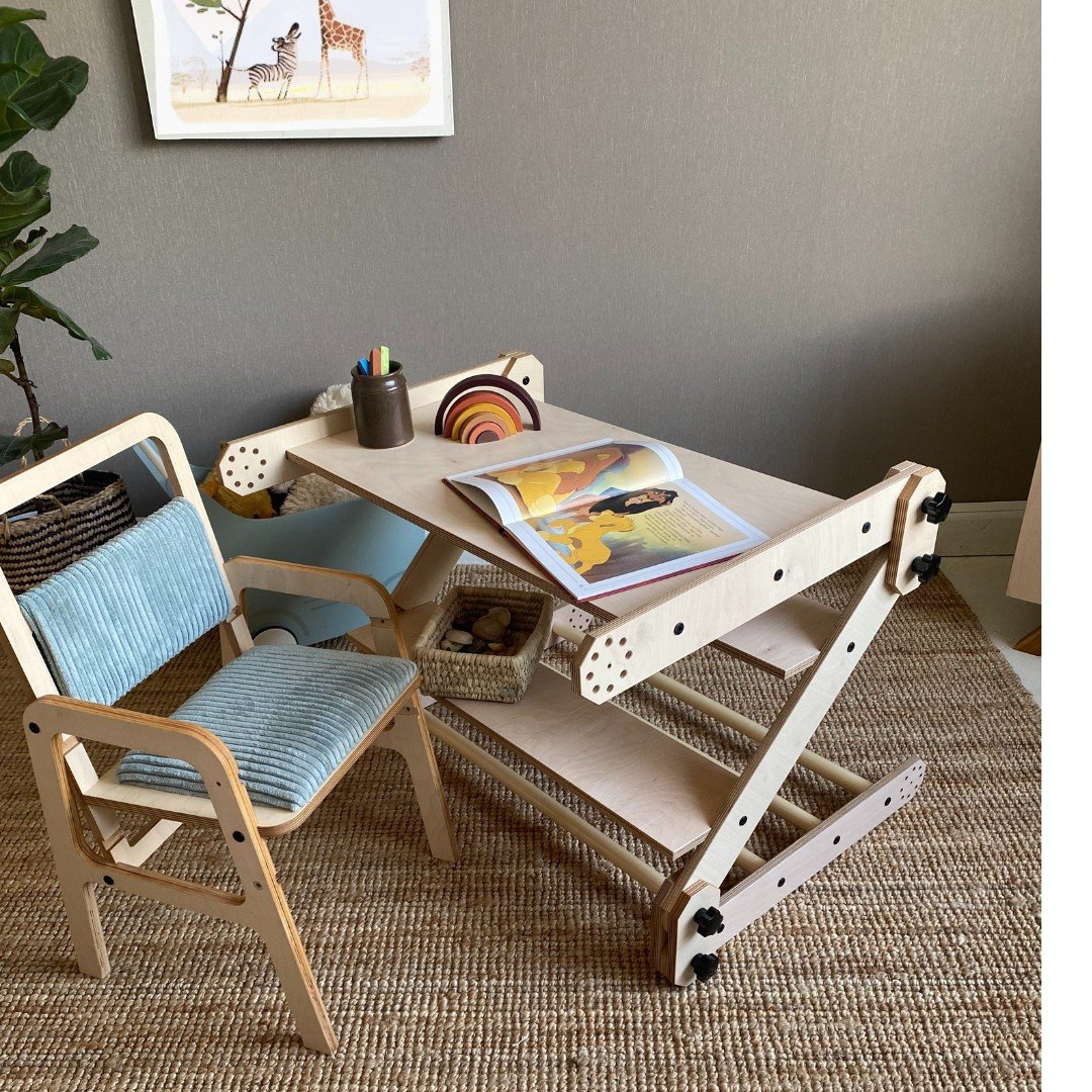 2. Montessori table setup with a wooden chair and drawing board, featuring a magazine and toys, in a modern playroom with a plant and wall art.
