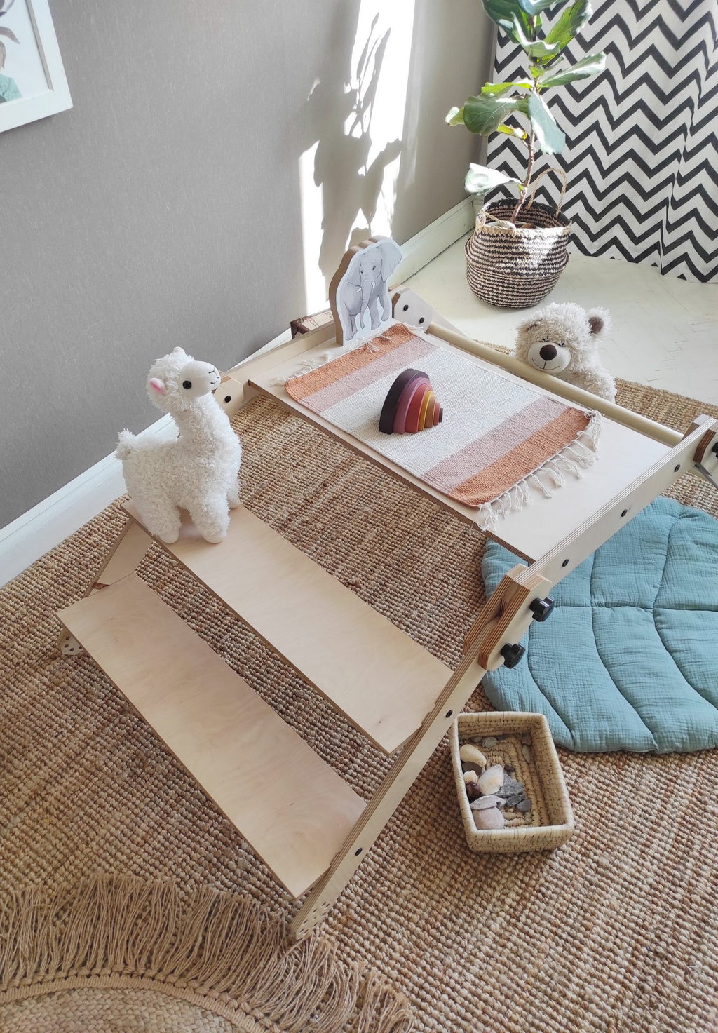 6. Montessori climbing set with a wooden ramp and plush llama, in a bright playroom with a chevron curtain and woven rug.