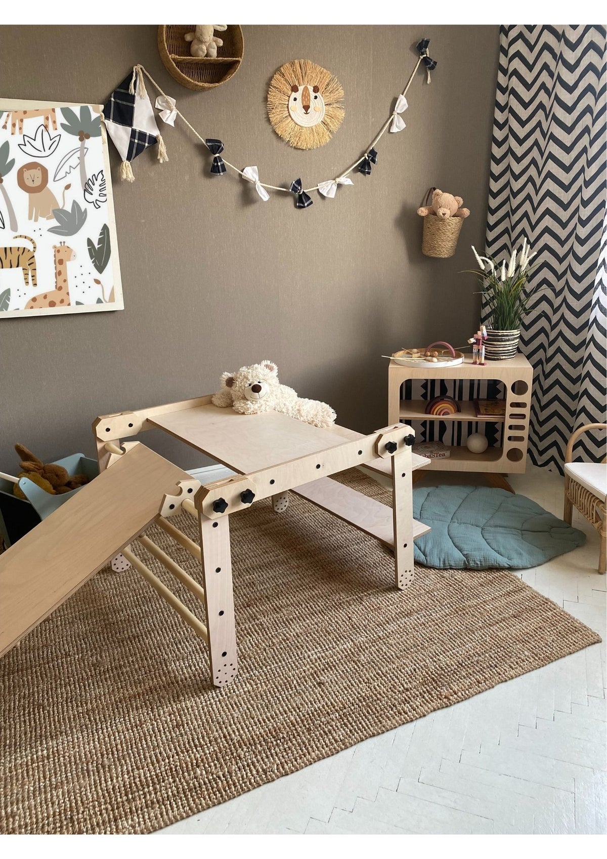 3. Montessori climbing set with a slide and table configuration, adorned with a teddy bear, in a stylish playroom with a chevron curtain.