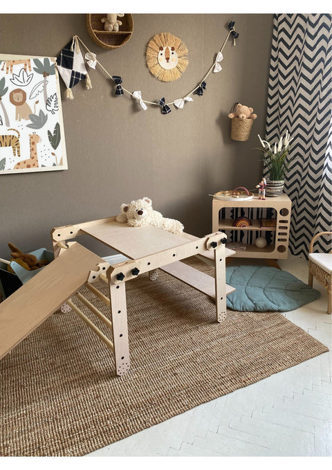 3. Montessori climbing set with a slide and table configuration, adorned with a teddy bear, in a stylish playroom with a chevron curtain.