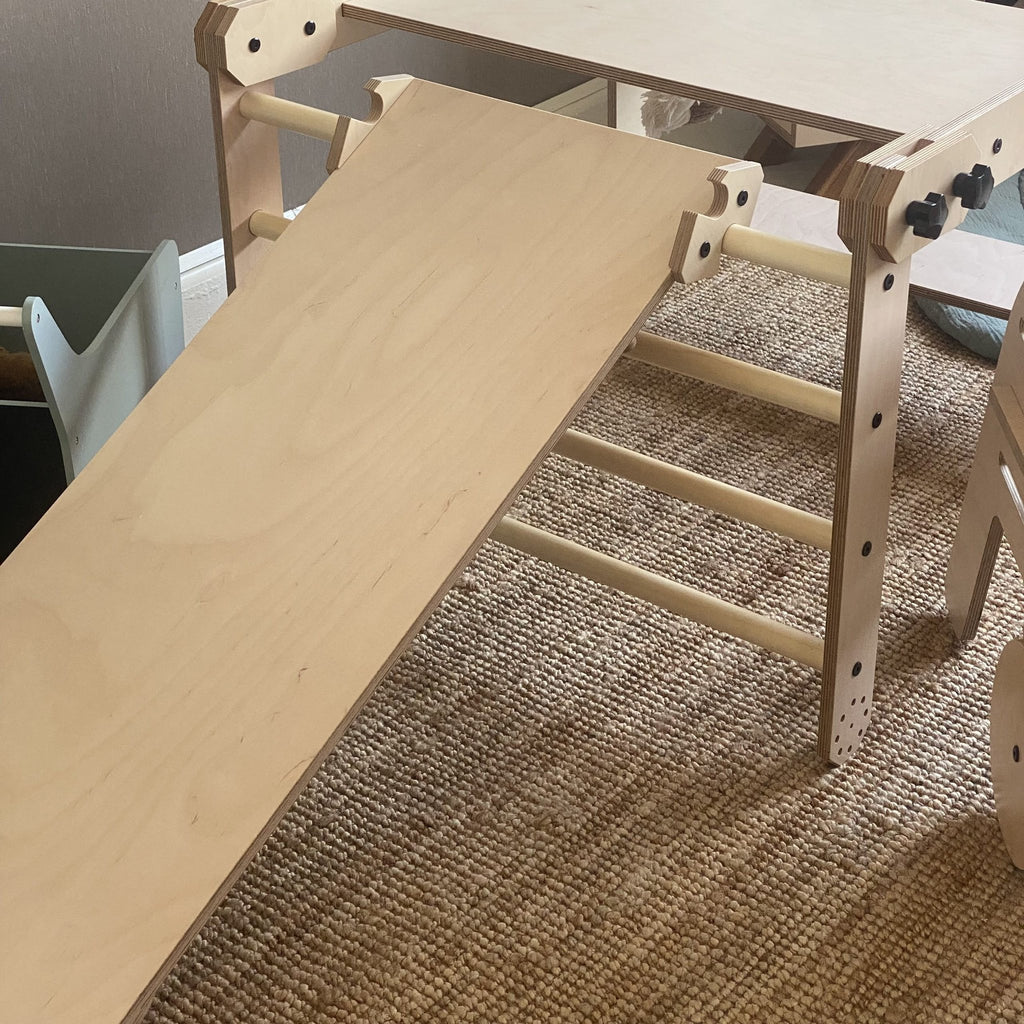 15. Montessori climbing set with a slide and table configuration, featuring plush toys, in a stylish playroom with a chevron curtain.